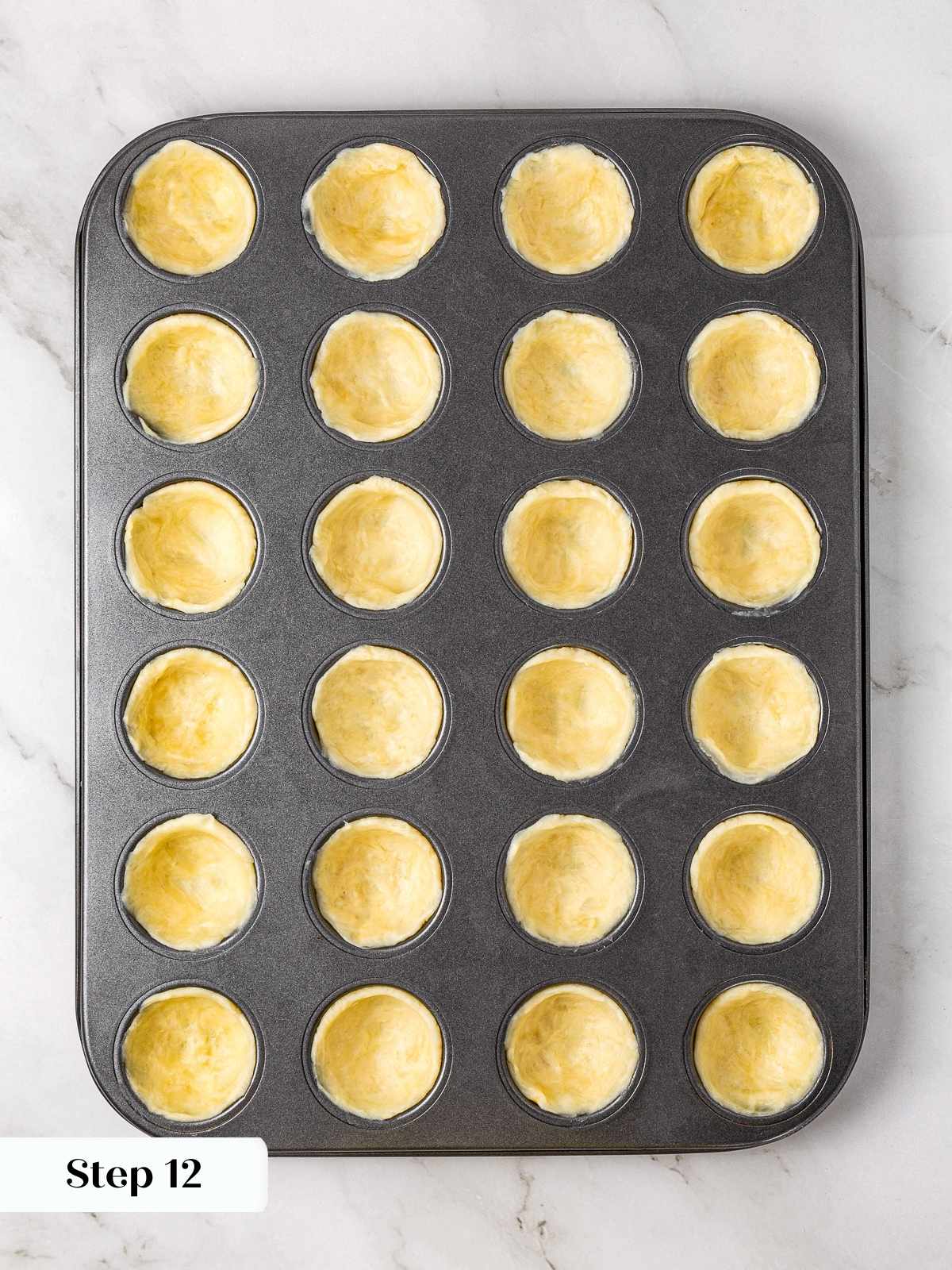 Dough pressed into muffin tin cavities forming the crusts for mini apple pies.