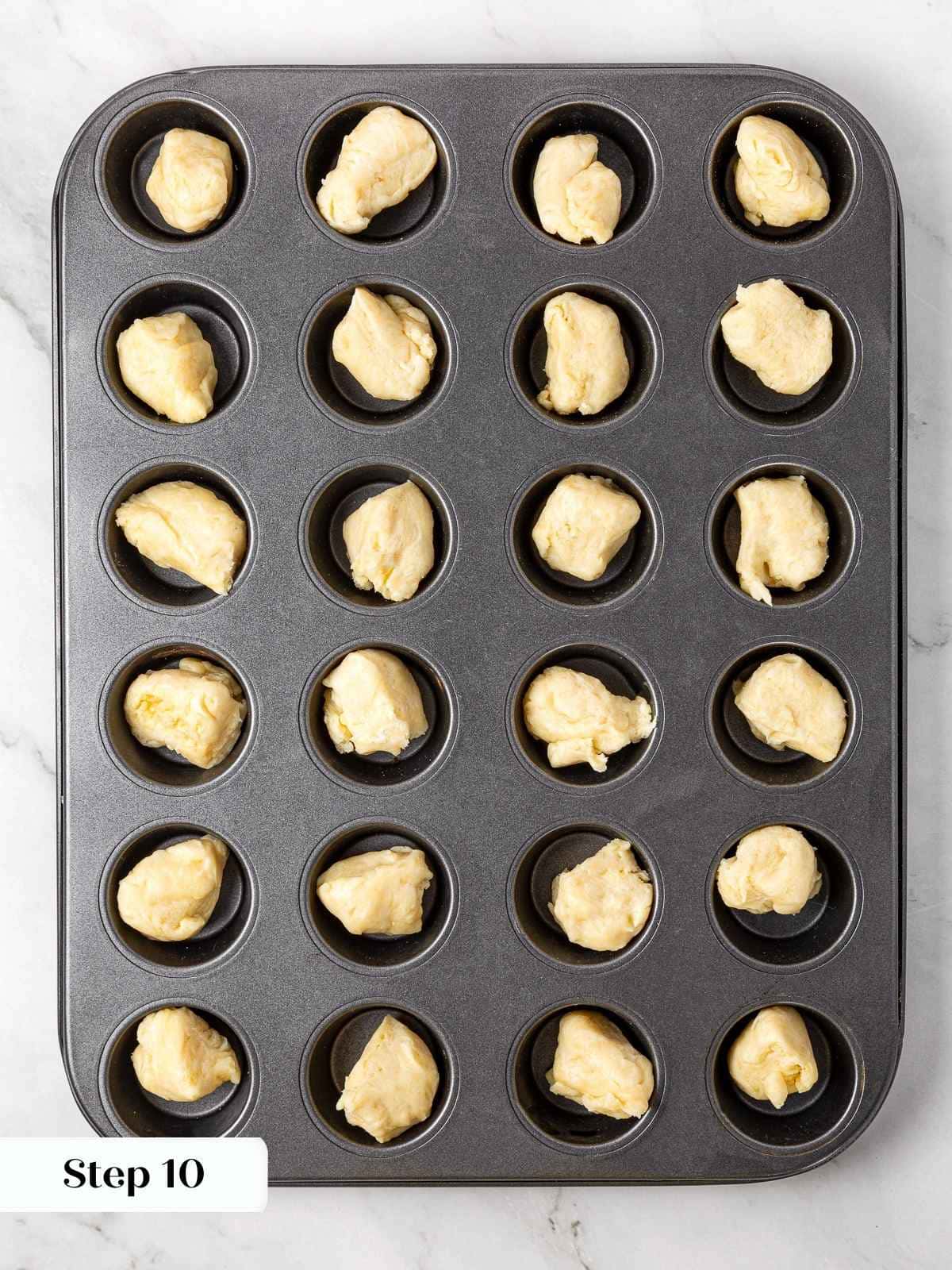 Pieces of dough placed into muffin tin cavities before pressing into crusts.