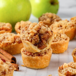 Baked mini apple pies arranged neatly on a white surface with crumble topping.
