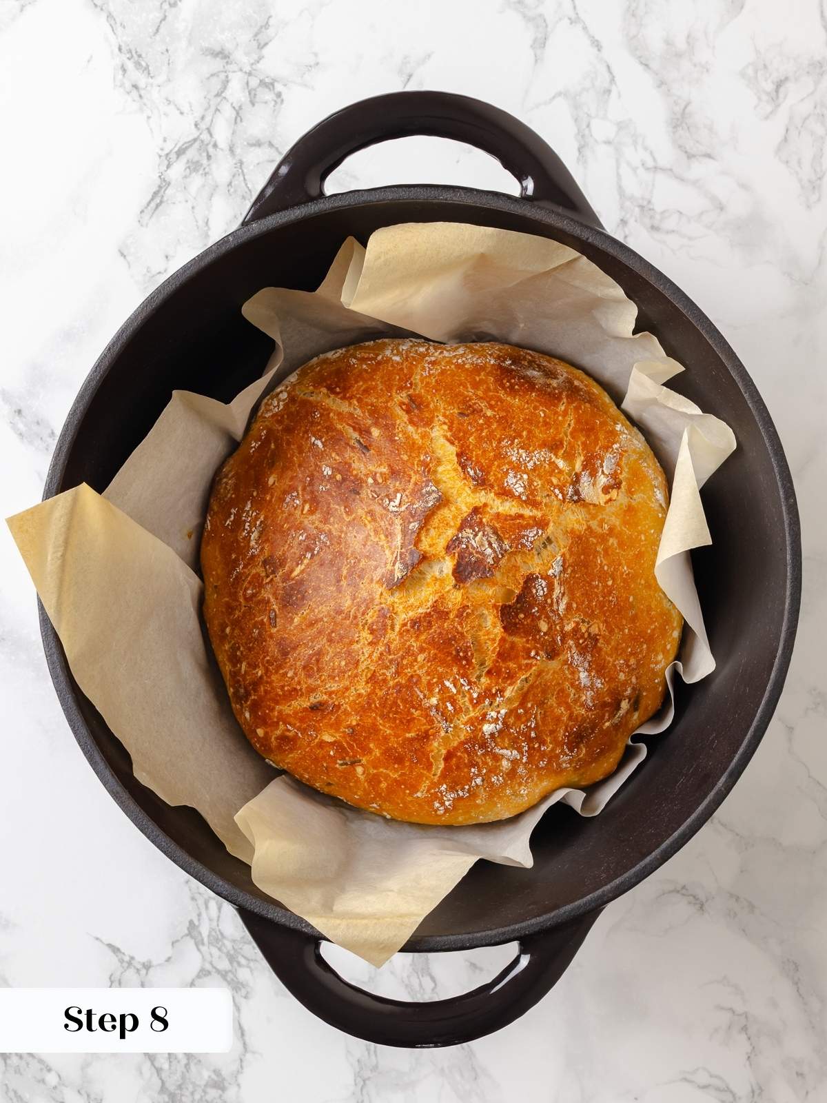 Golden rosemary bread loaf cooling inside Dutch oven after baking, with lid removed.
