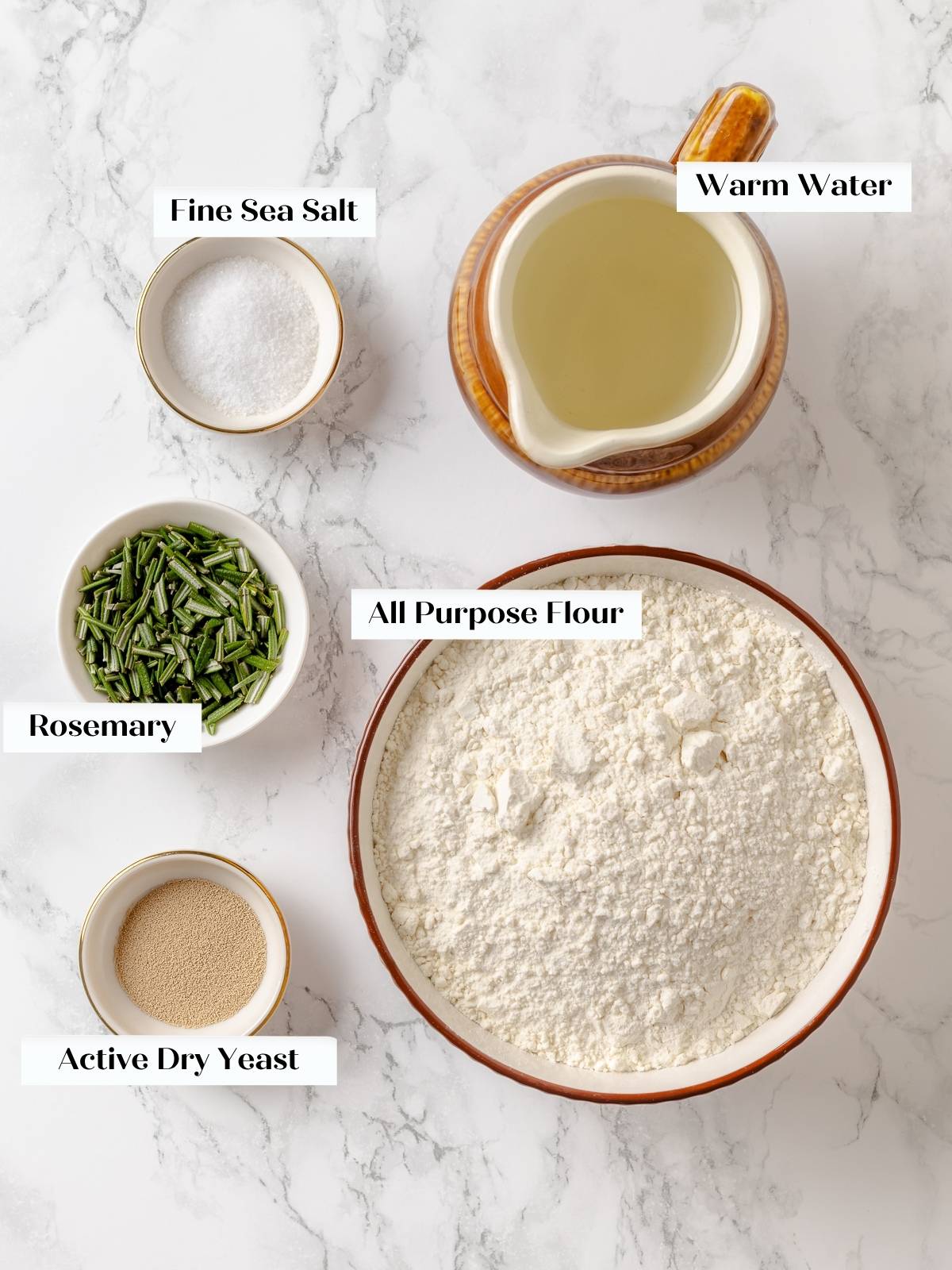 Ingredients for rosemary bread including flour, salt, yeast, and rosemary laid out on a kitchen counter.