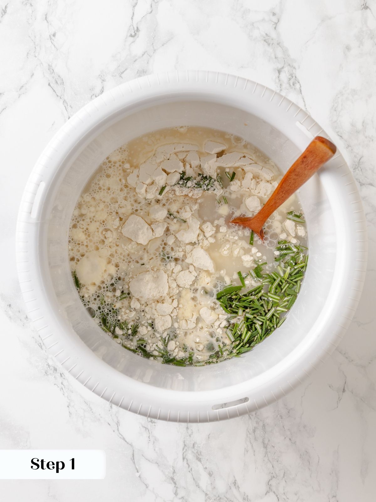 Mixing bowl filled with flour, rosemary, and yeast while preparing homemade rosemary bread dough.