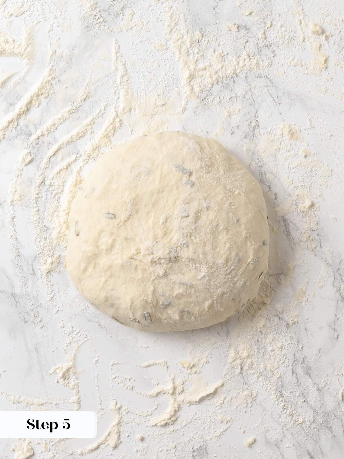 Shaped round dough for rosemary bread resting on counter before baking.