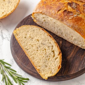 Rustic loaf of rosemary bread sliced open to reveal airy, uneven crumb and baked herbs.