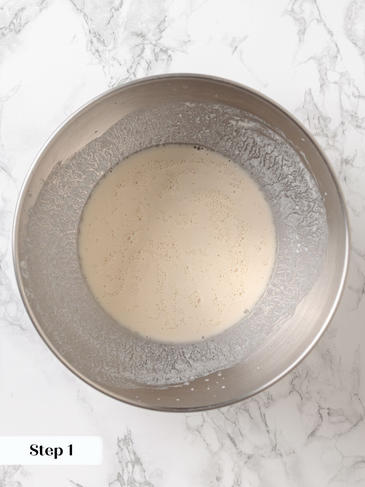 Frothy yeast mixture in a bowl showing active bubbles for making dinner roll dough.
