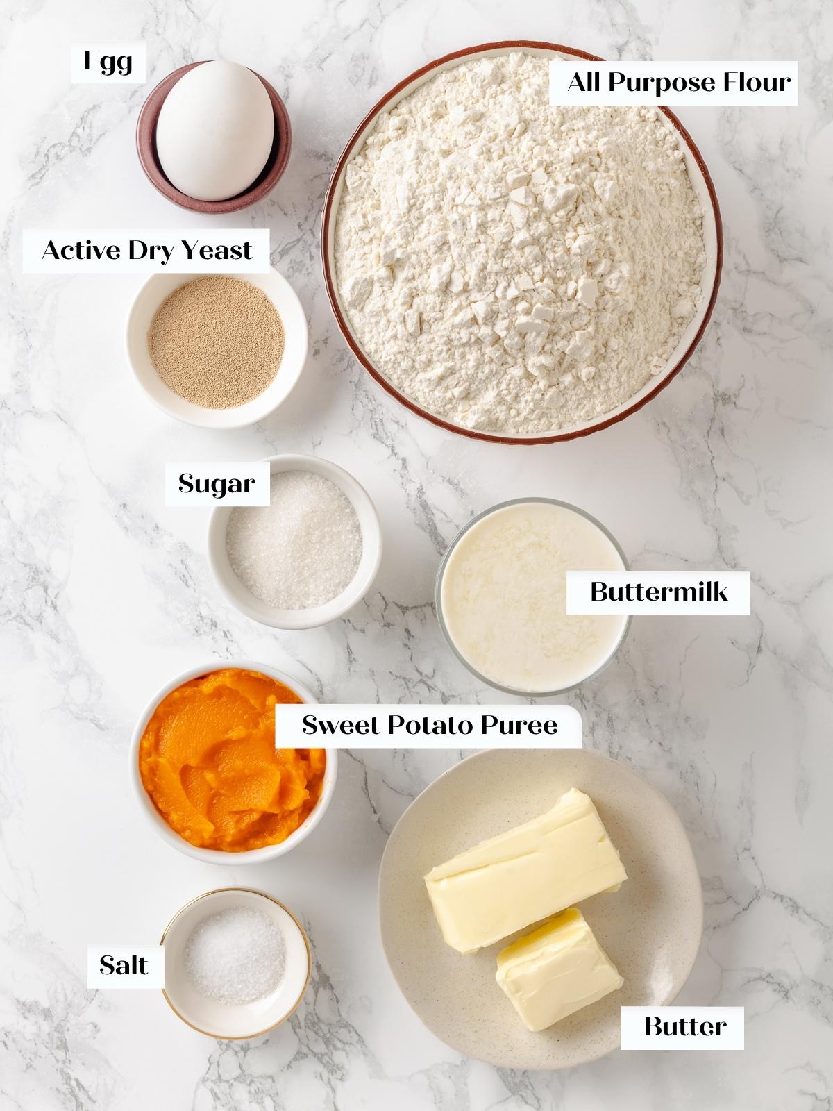 Ingredients for sweet potato dinner rolls arranged on a kitchen counter including flour, eggs, and butter.