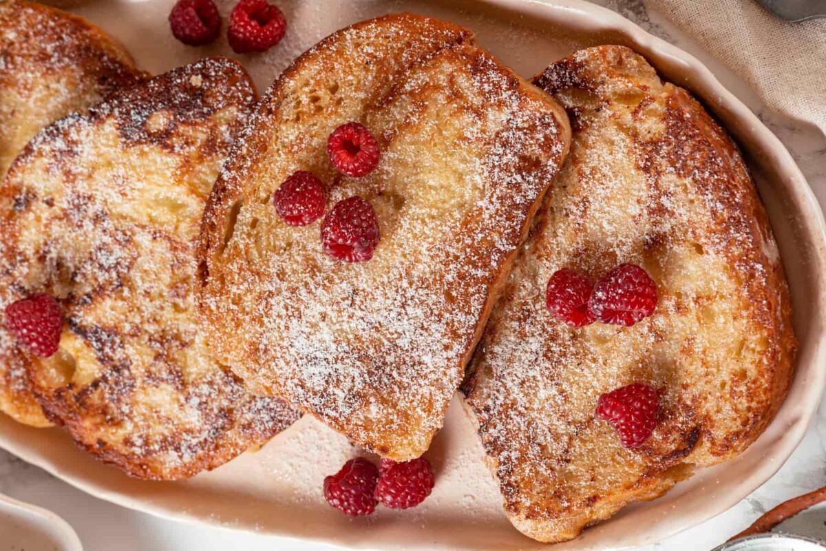 Slices of brioche French toast topped with powdered sugar and fresh raspberries ready to serve.