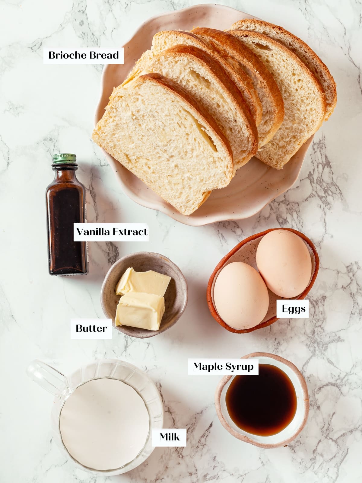Eggs, milk, brioche bread, and maple syrup arranged on a countertop before making French toast.