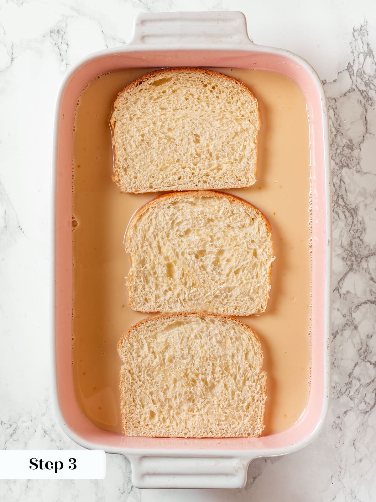 Thick brioche bread slices resting in a dish of custard to soak before cooking.