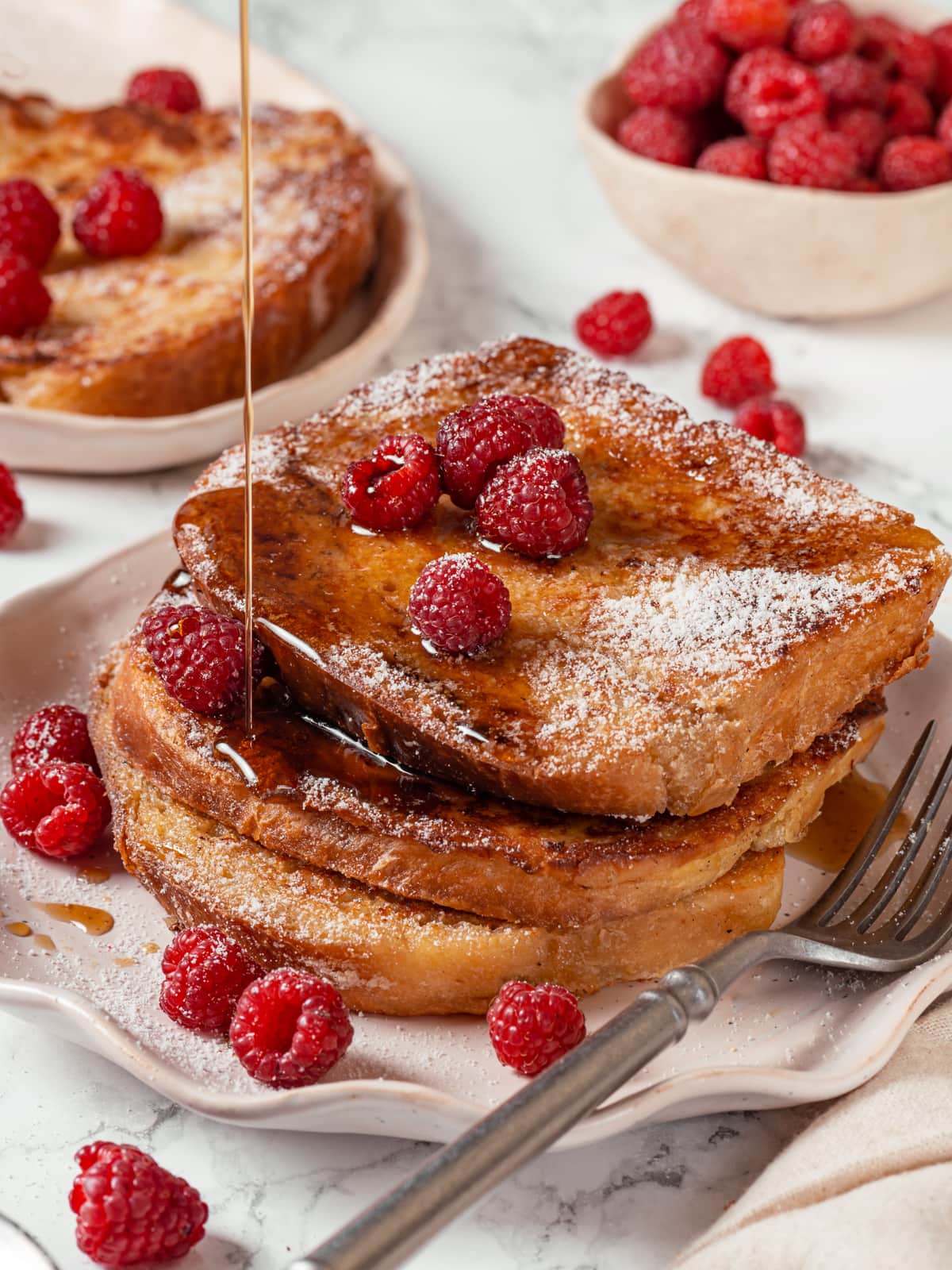 Maple syrup dripping slowly down the side of a thick slice of brioche French toast.