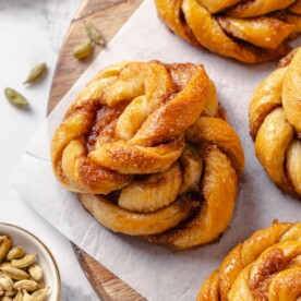 Whole green cardamom pods scattered beside freshly baked buns.