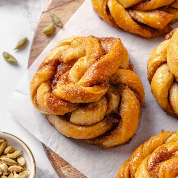 Whole green cardamom pods scattered beside freshly baked buns.