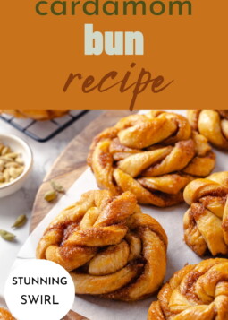 Knotted cardamom buns cooling on a cutting board with bits of cinnamon filling visible between folds.