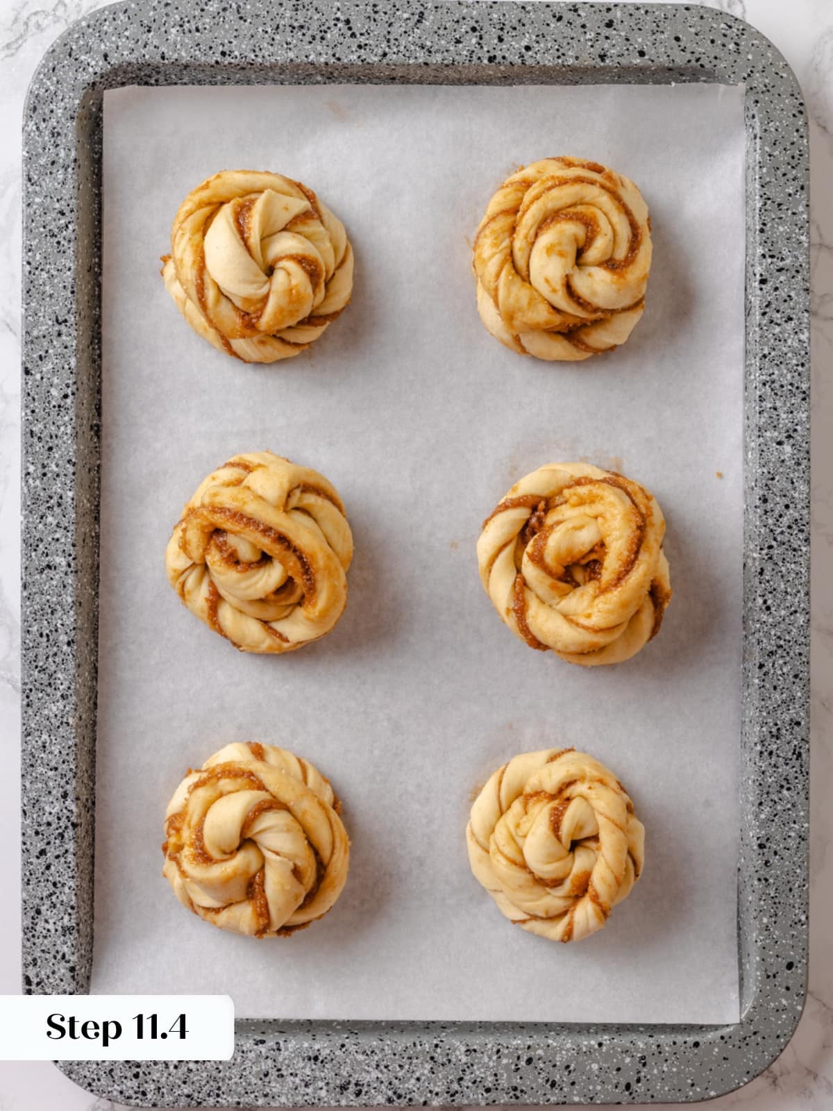 Twisted cardamom buns arranged on a parchment-lined baking sheet before baking.