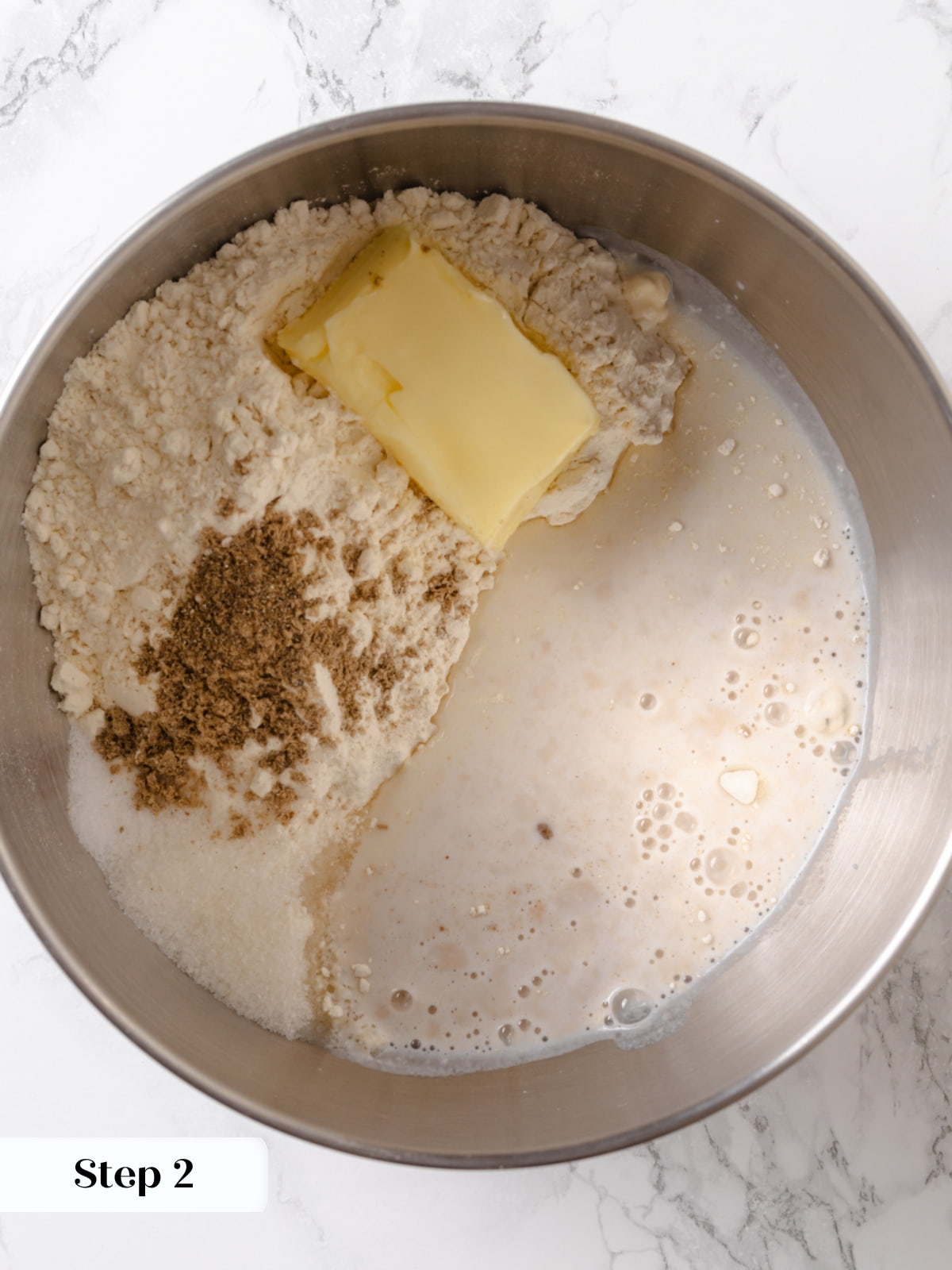 Combining flour, sugar, cardamom, and yeast mixture in mixer to start dough formation.