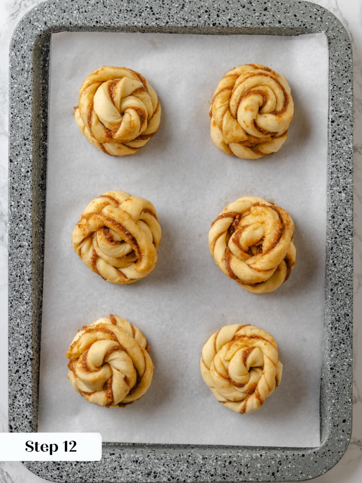 Twisted cardamom buns resting on baking trays during their final proof before baking.