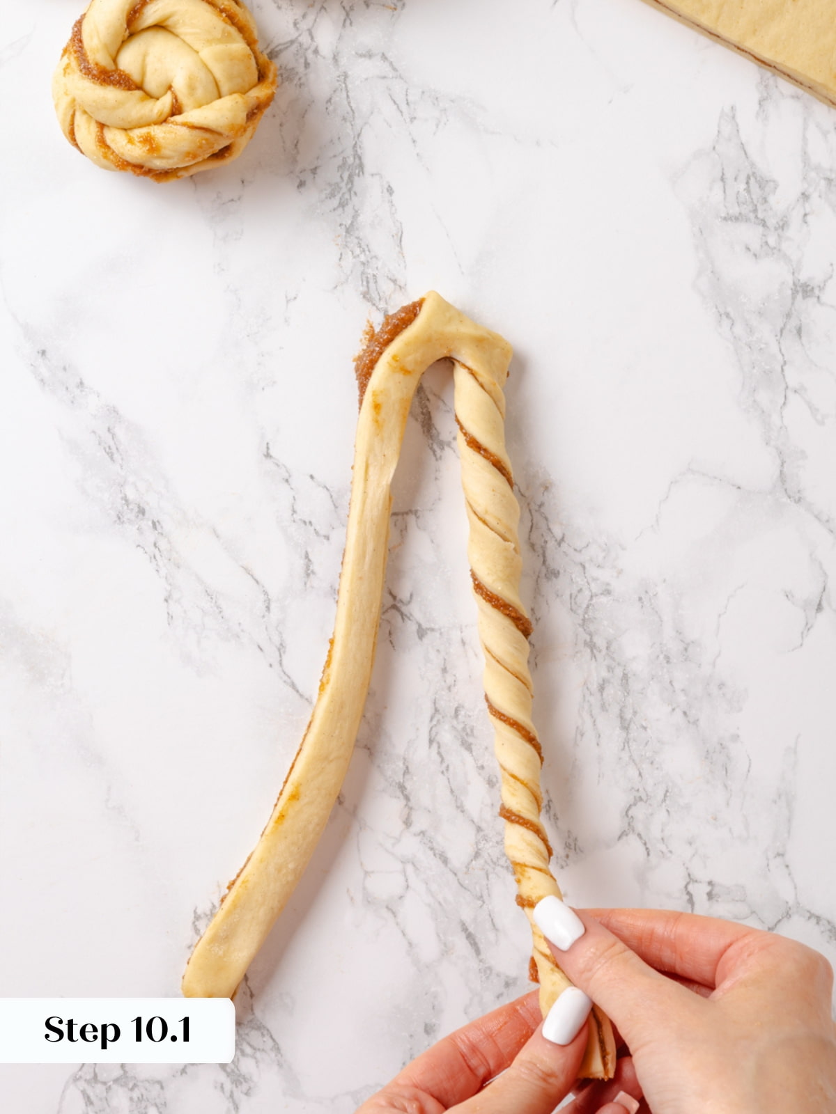 The right dough strand being twisted tightly to create spiraled layers filled with cinnamon.