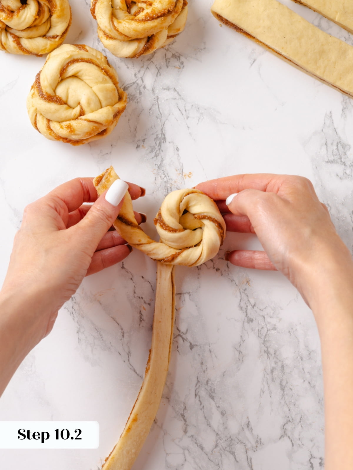 Twisting the right strand of dough around the bun&rsquo;s base to form the knot.