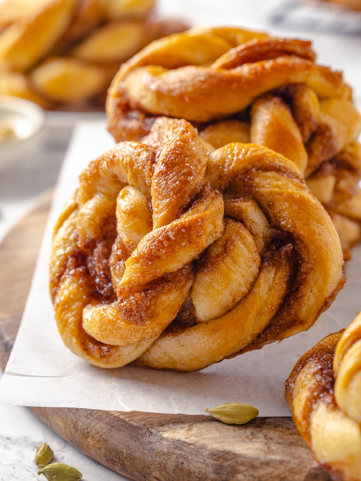 Pair of baked cardamom buns with shiny syrup glaze and visible twisted folds.