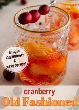 Cranberry old fashioned cocktail in a glass with ice cubes, and garnished with orange peel and cranberries.