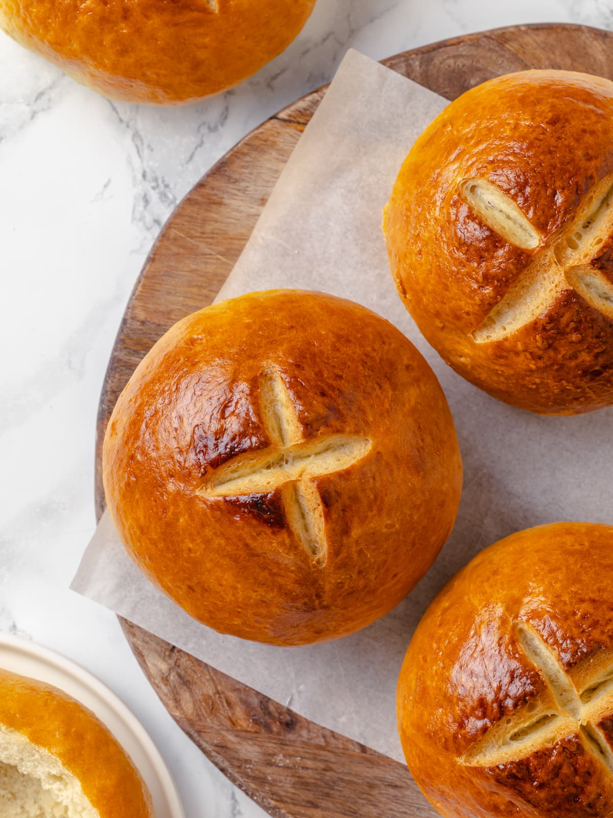 Golden bread rolls resting on parchment lined tray after baking.
