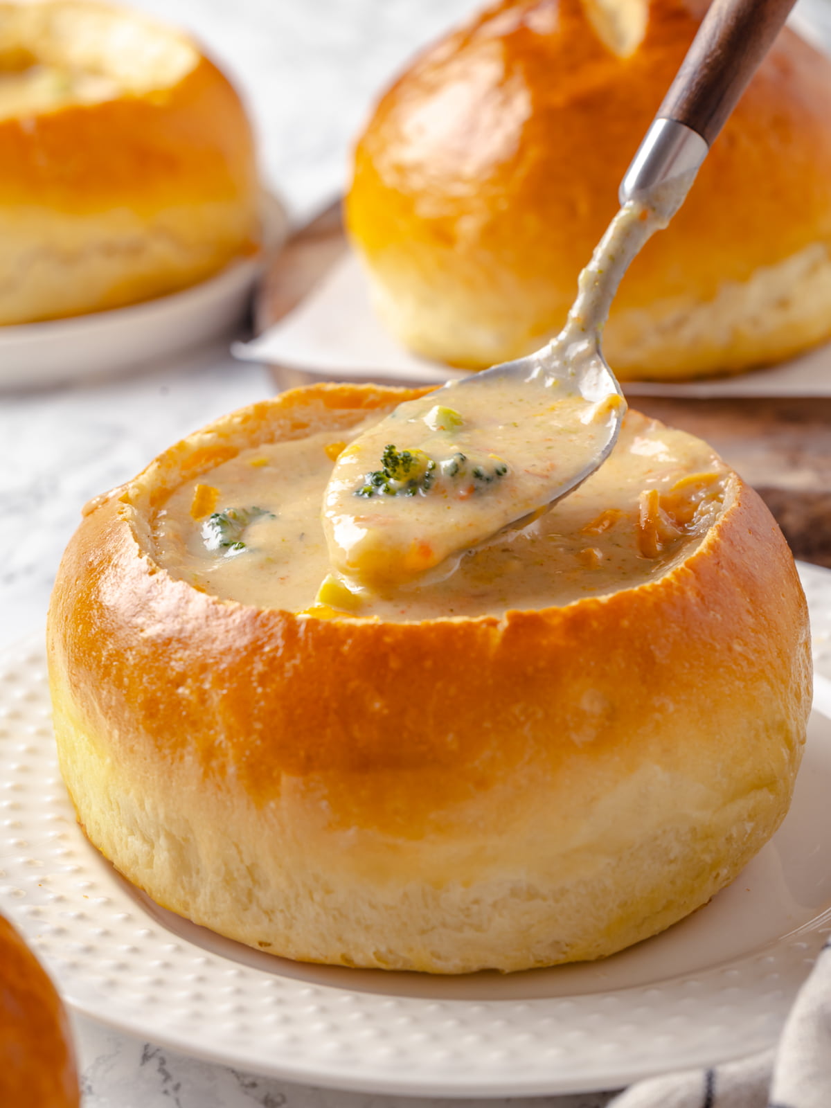 Spoon lifted from a bread bowl showing warm soup dripping back into the center.