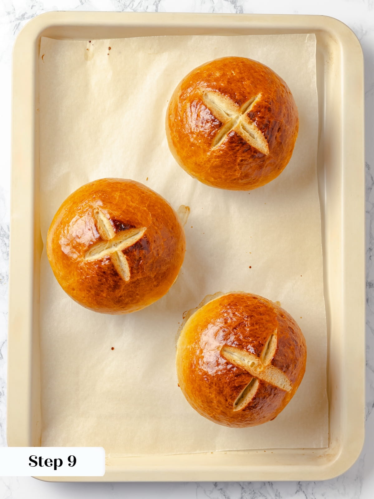 Freshly baked bread bowls resting on a sheet after coming out of the oven.