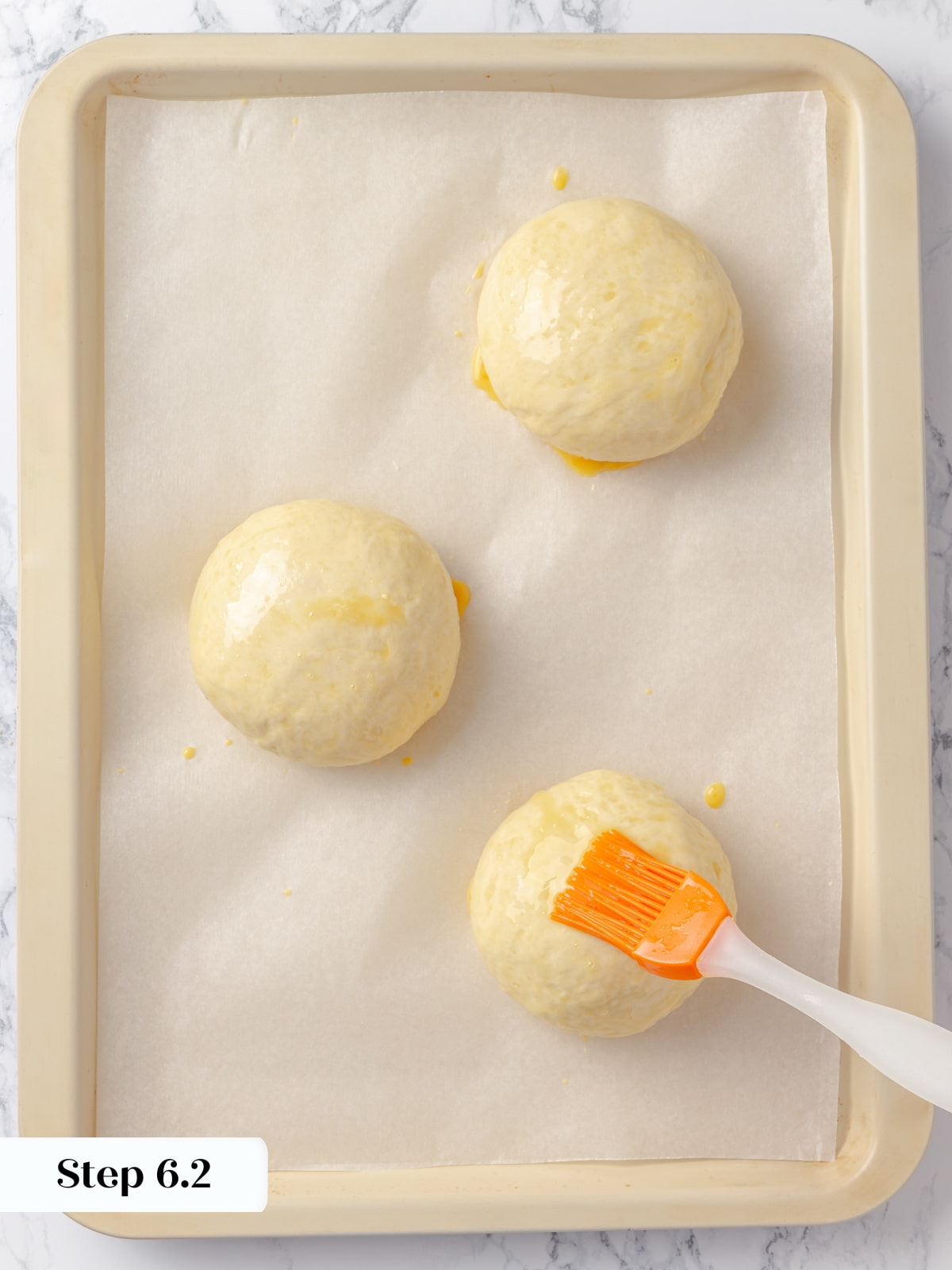 Dough balls being brushed with egg wash to create a shiny golden top when baked.