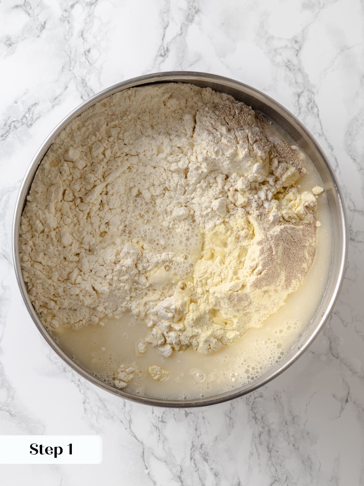 Bread dough ingredients beginning to combine in a mixing bowl to form a smooth dough.