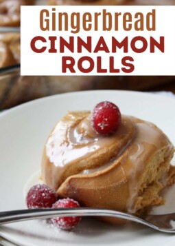 Plate with a golden brown gingerbread cinnamon roll topped with silky cinnamon-vanilla glaze and a sugared cranberry.