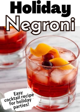 Holiday negroni cocktail in a glass with ice cubes, and garnished with orange peel and cranberries.