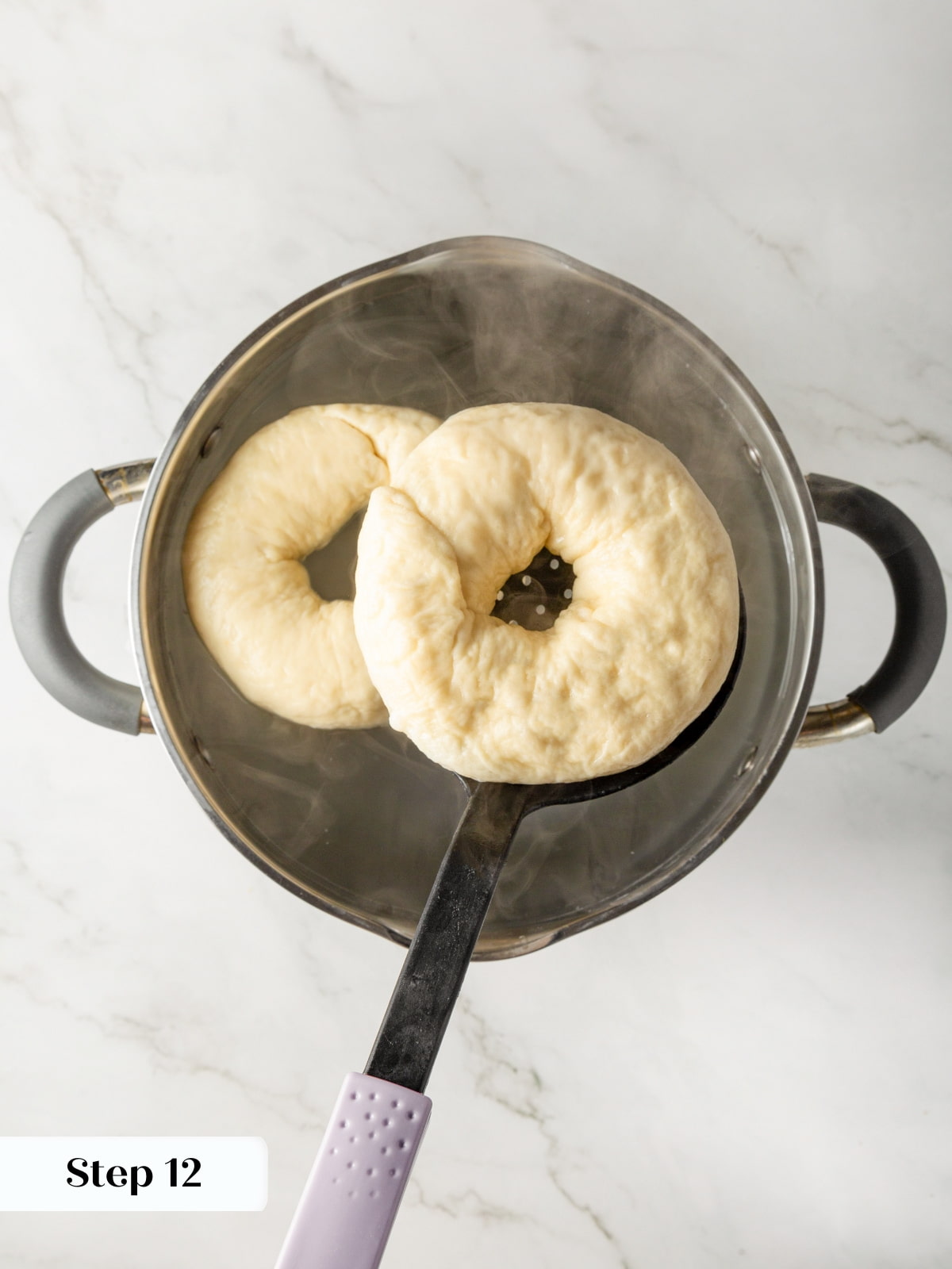 Bagels cooking in simmering water as one is turned to finish poaching evenly.