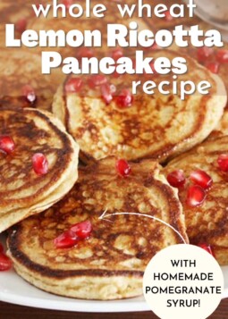 Golden brown lemon ricotta pancakes on a plate topped with pomegranate syrup and bright red pomegranate seeds.