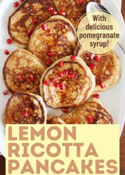 Golden brown lemon ricotta pancakes on a plate topped with pomegranate syrup and bright red pomegranate seeds.