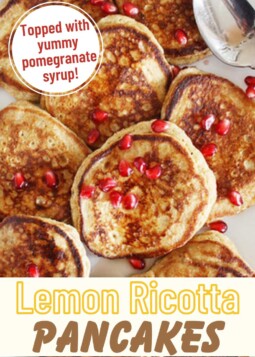 Golden brown lemon ricotta pancakes on a plate topped with pomegranate syrup and bright red pomegranate seeds.