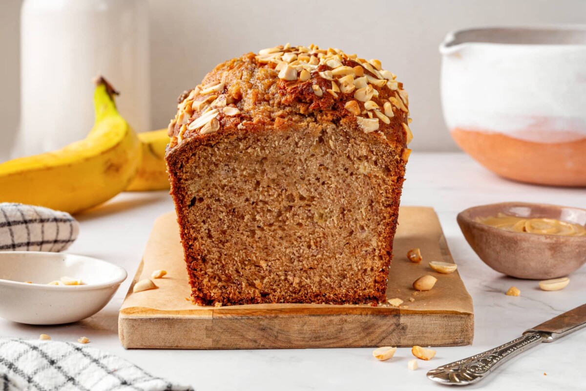 Freshly baked peanut butter banana bread loaf resting on a wooden board ready to slice.