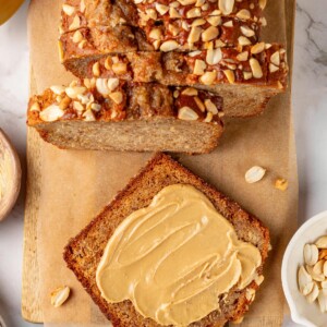 Slice of banana bread coated with creamy peanut butter for a rich, warm snack moment.