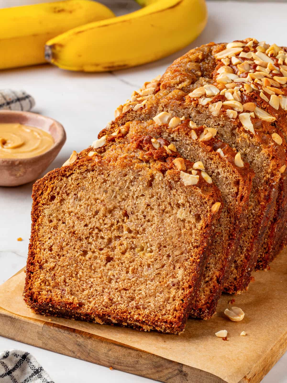 Banana bread slices shown with whole bananas behind them highlighting fresh ingredients.