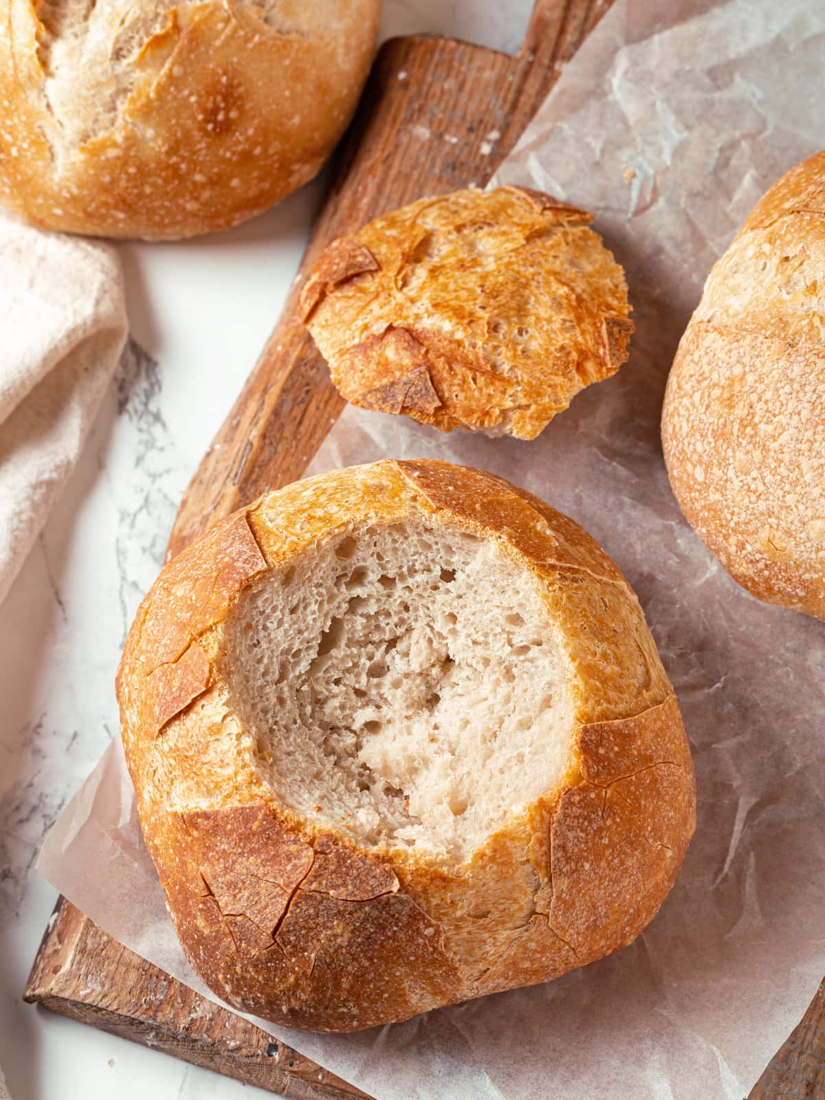 Sourdough bread bowl with top removed and interior hollowed, placed beside sliced bread.