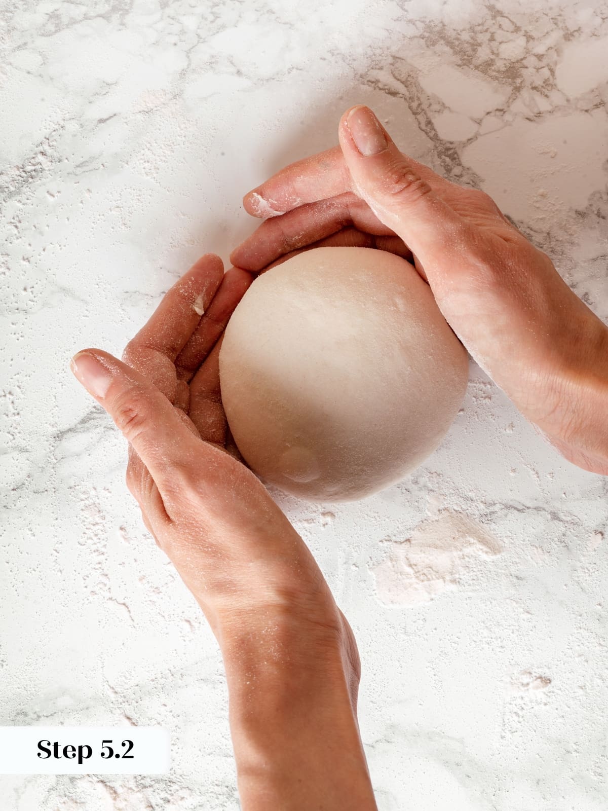 Hands pulling dough across surface to create a tight round boule.