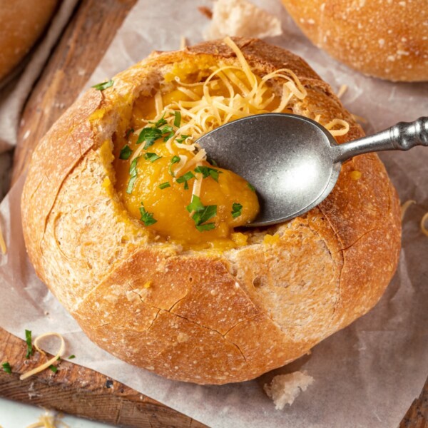 Spoon lifting soup from inside a sturdy sourdough bread bowl.