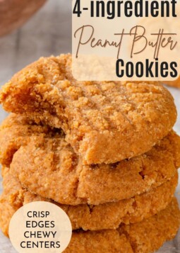 Stack of chewy peanut butter cookies with fork marks cooling on parchment paper after baking.