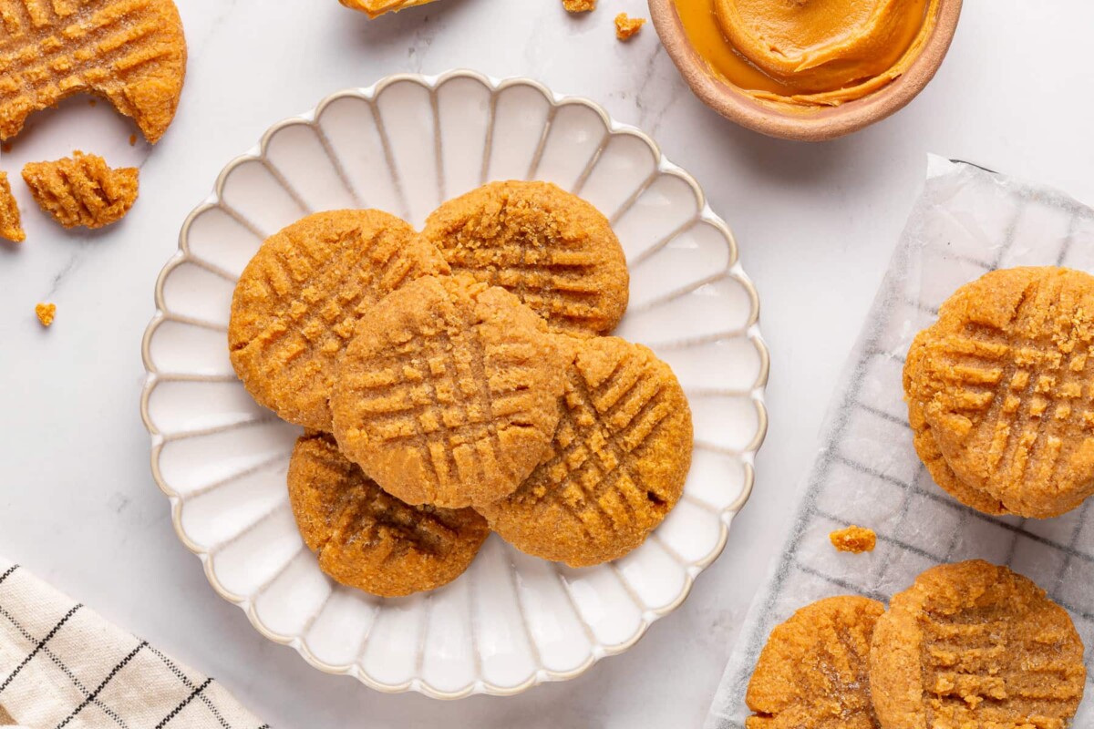 Four ingredient peanut butter cookies arranged on a white plate with visible fork marks.