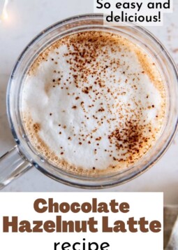 Warm chocolate hazelnut latte topped with cocoa powder held in a glass mug.