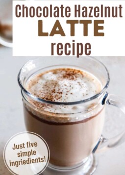 Warm chocolate hazelnut latte topped with cocoa powder held in a glass mug.
