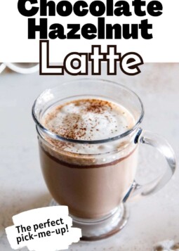 Warm chocolate hazelnut latte topped with cocoa powder held in a glass mug.