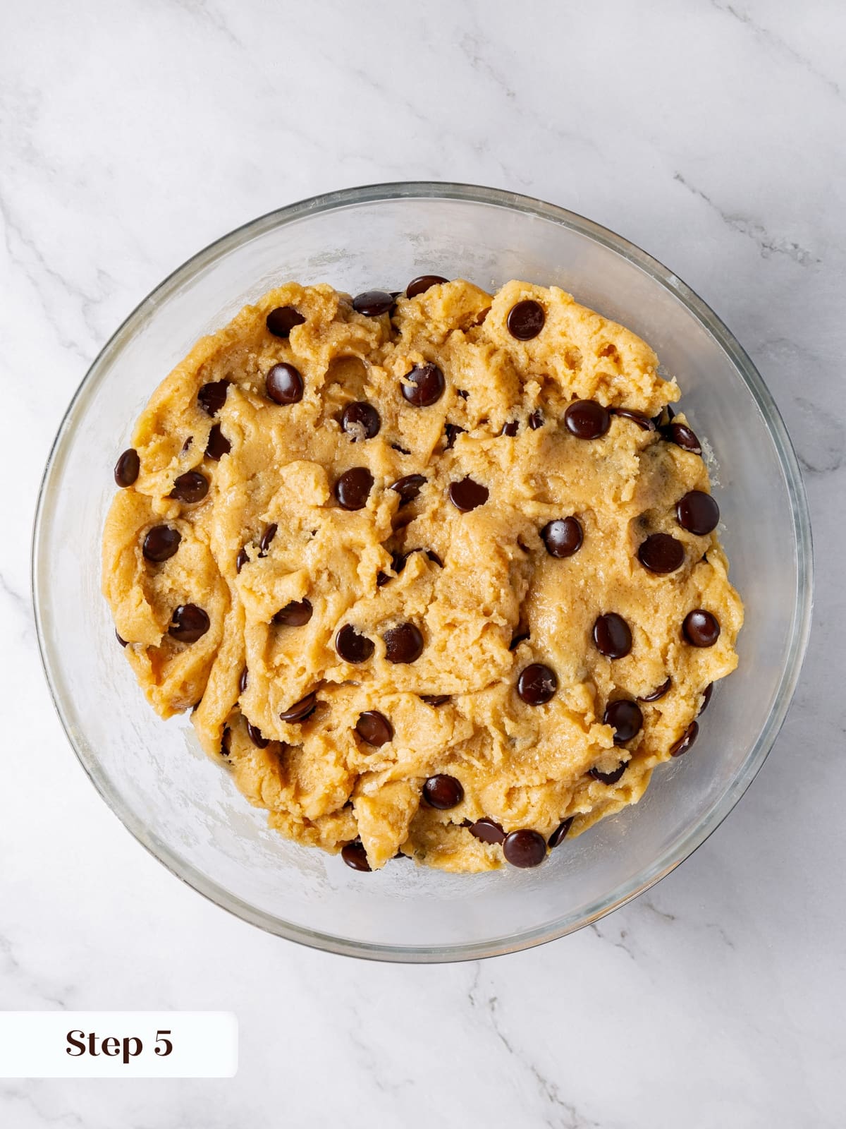 Dark chocolate chips being added to sourdough cookie dough before mixing.