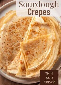 Stack of paper thin sourdough crêpes with golden crispy edges resting on a plate.