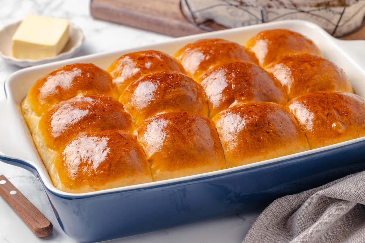 Golden dinner rolls baked in a blue dish with puffed tops and soft sides.