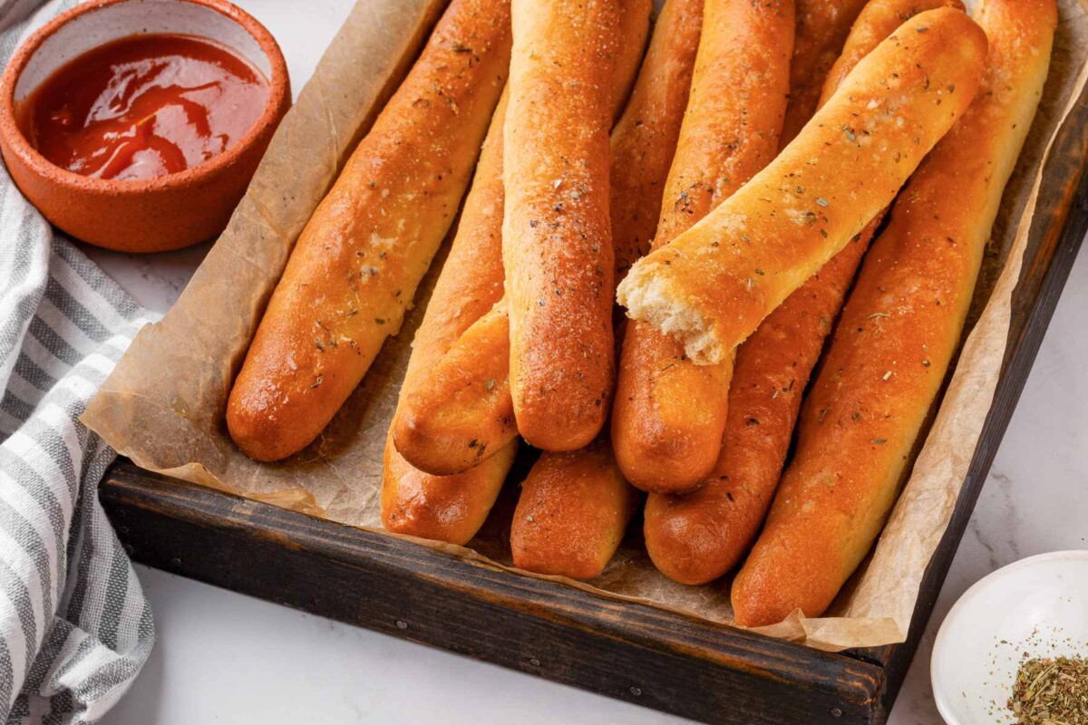 Garlic breadsticks served beside bowl of marinara sauce for dipping.